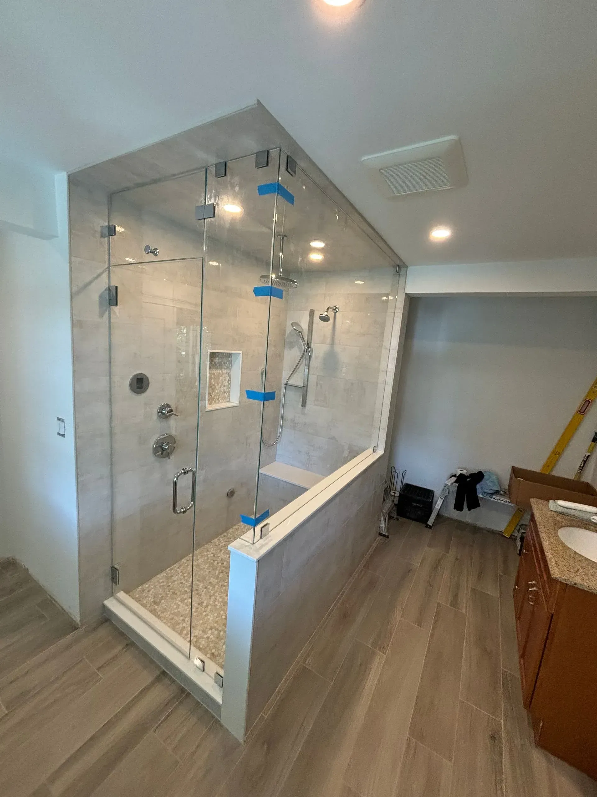 Modern, tiled shower with glass doors, a bench, and multiple shower heads.