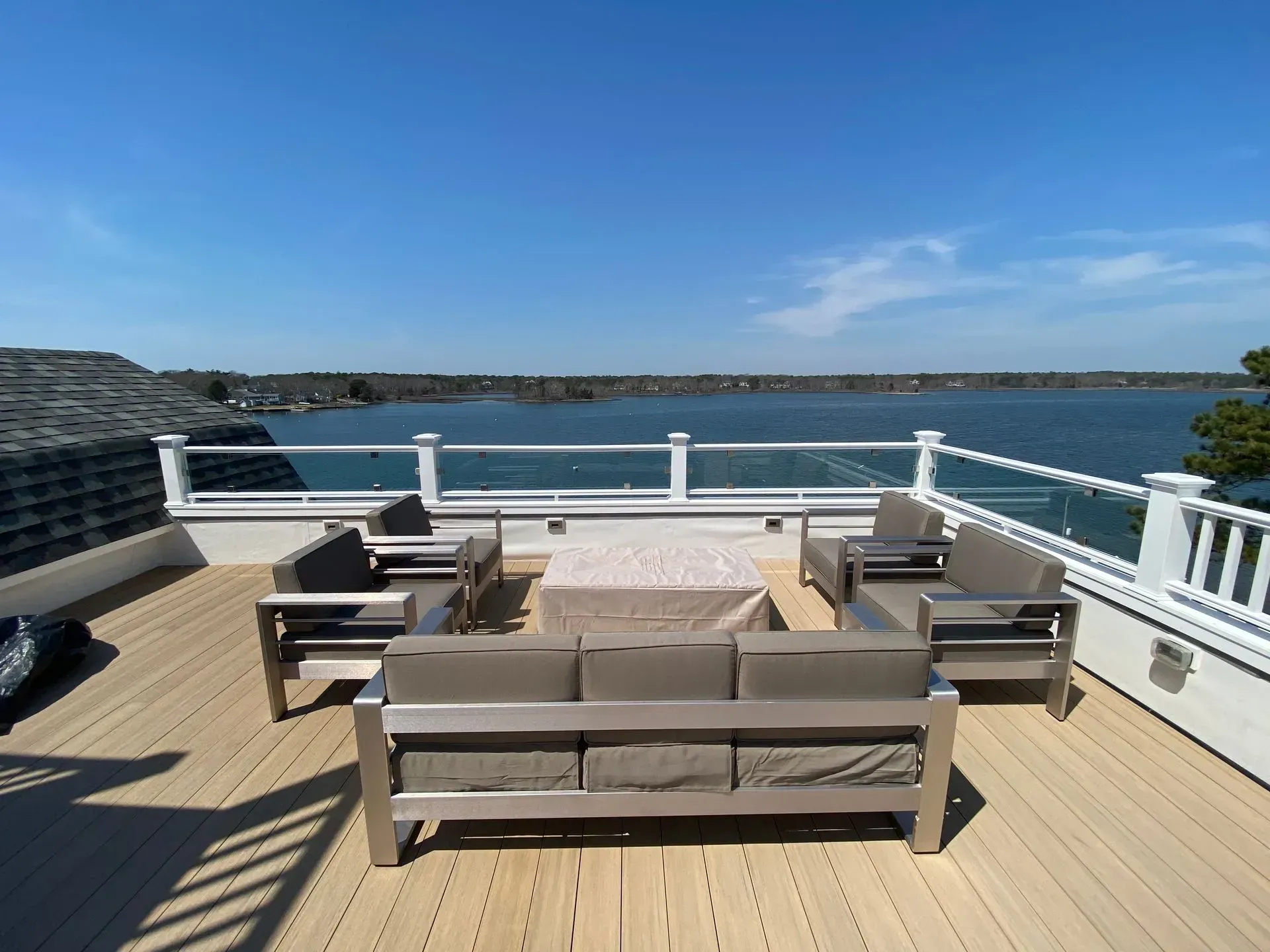 Outdoor deck with metal furniture, overlooking water and blue sky.