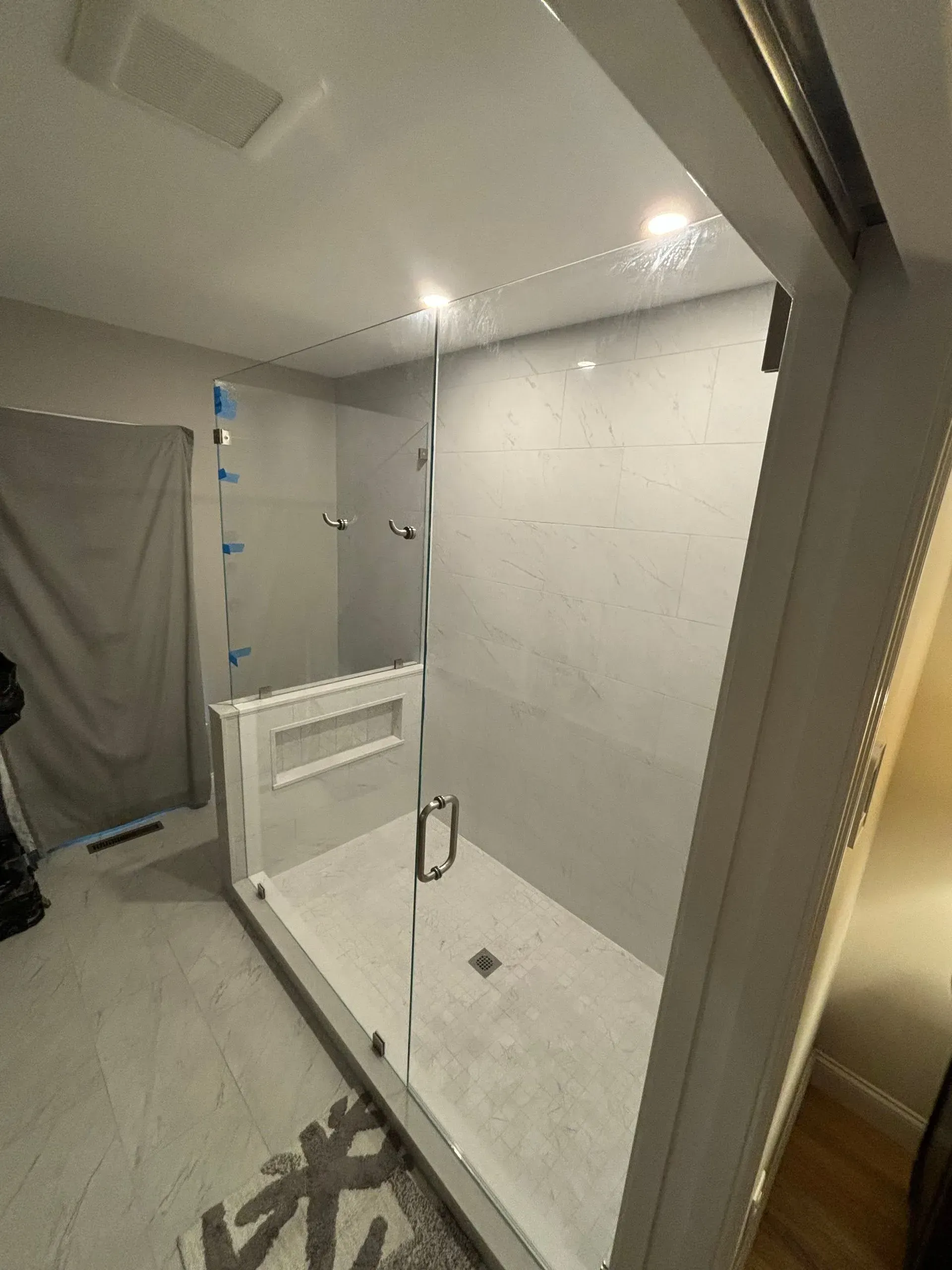 A modern bathroom with a glass shower, light gray tiles, and a white vanity.
