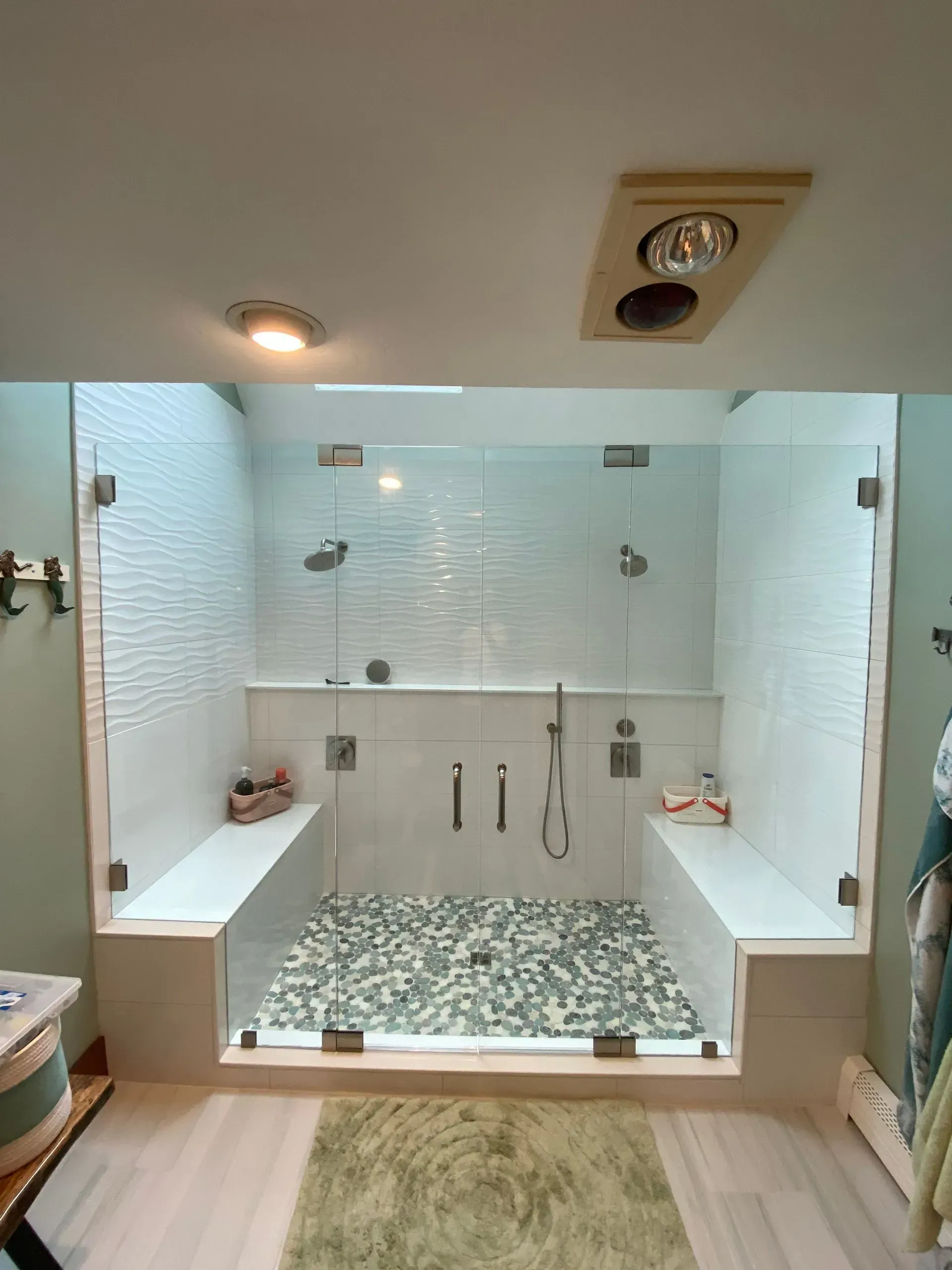 Spacious, modern shower with glass doors, pebble floor, white tile, and built-in benches.