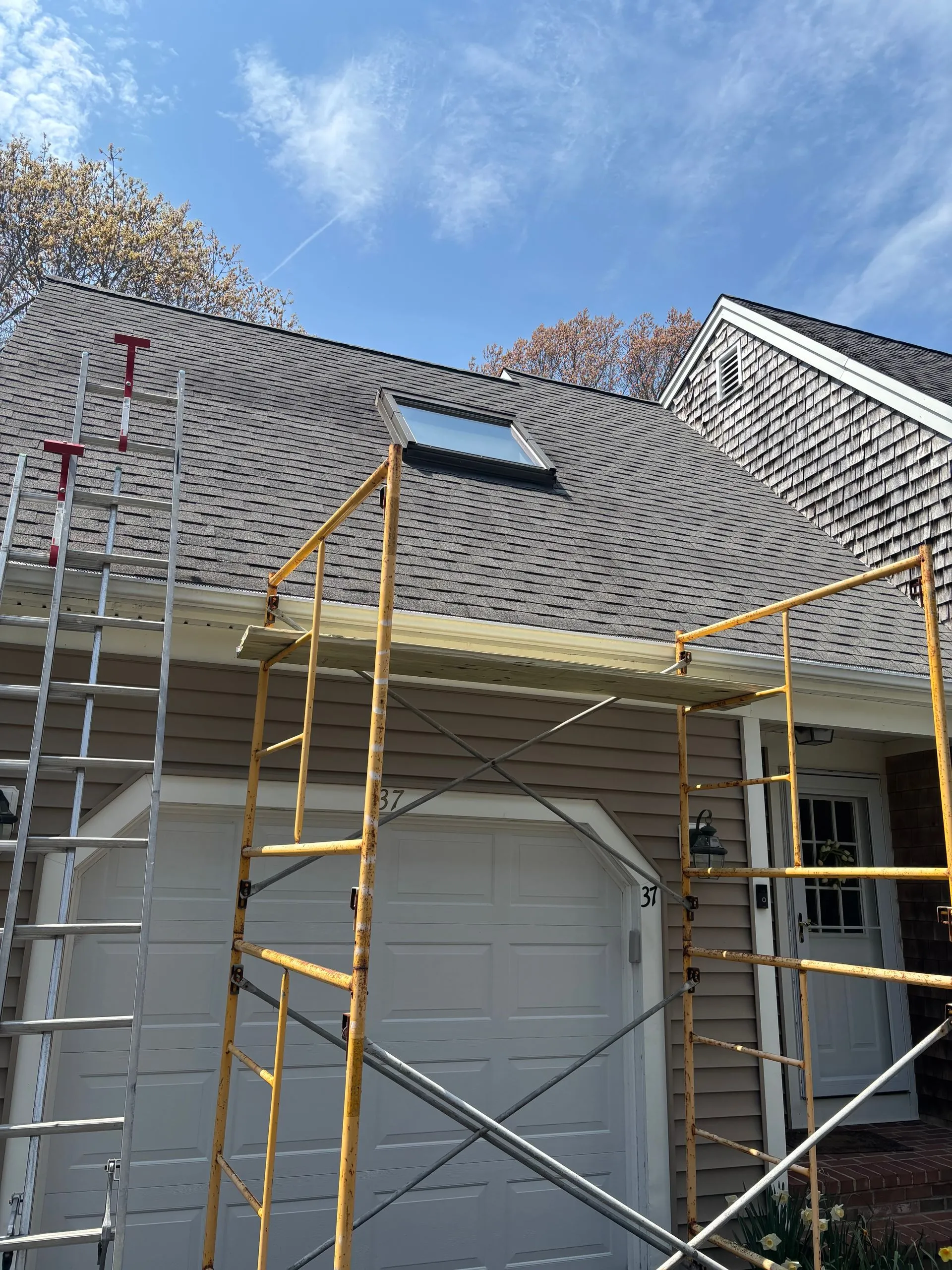 Scaffolding by a garage with a dark roof and skylight on a sunny day.