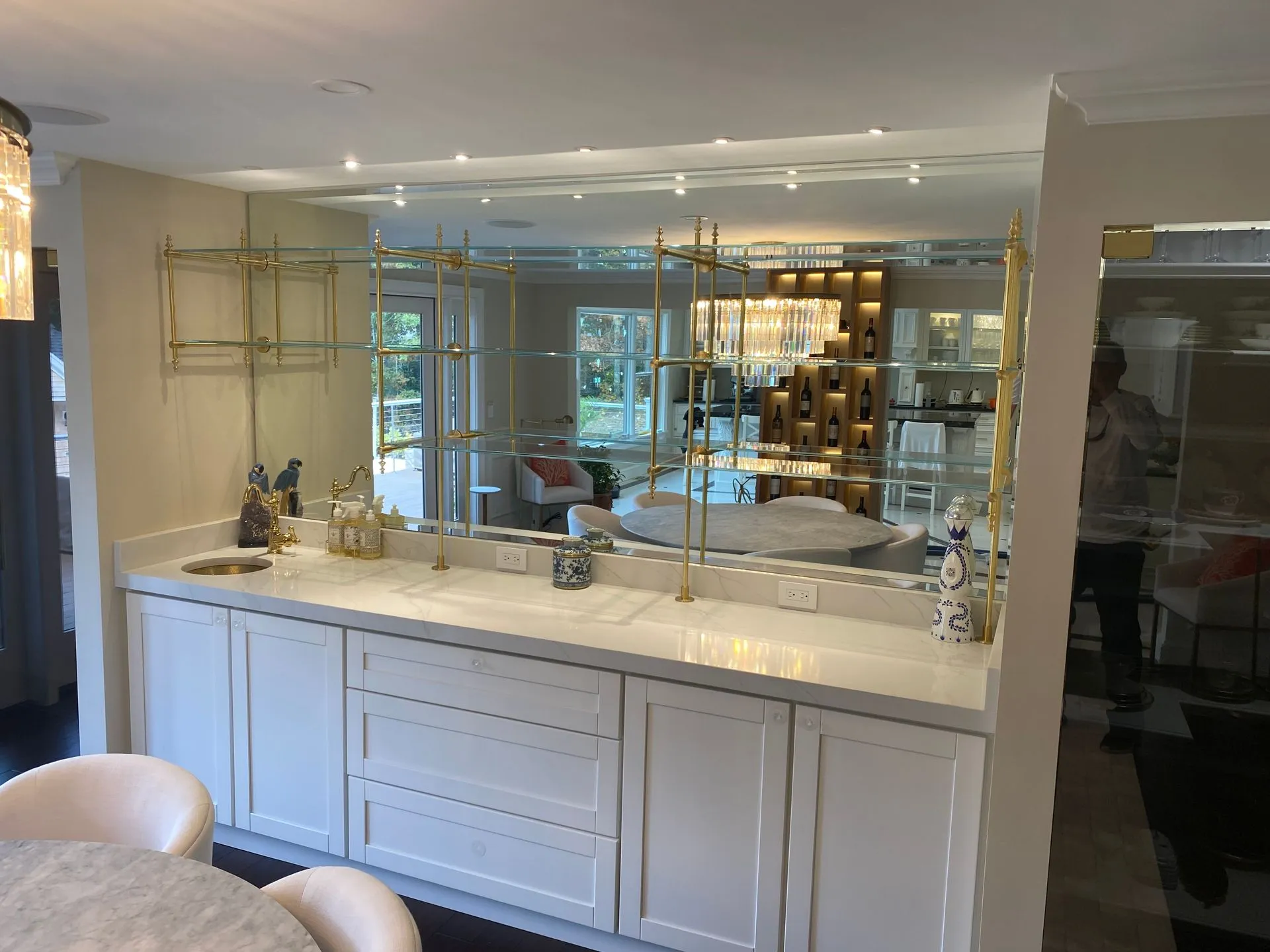 White cabinetry with marble countertop and gold shelving, reflecting interior with a modern staircase.