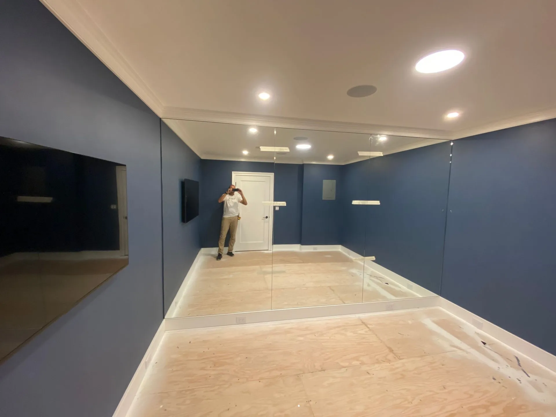 Man in a room with blue walls, a large mirror, and a wooden floor.