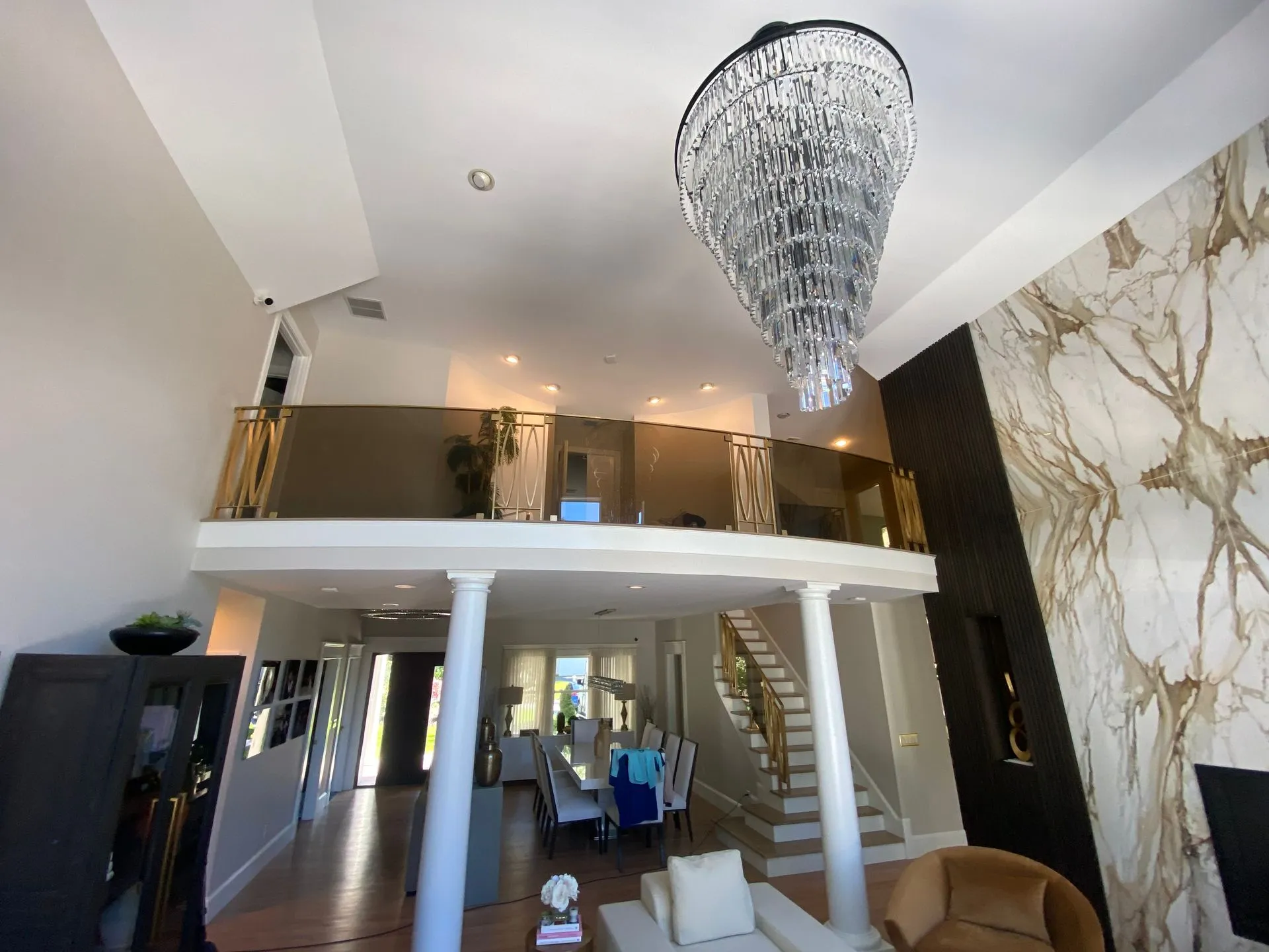 Luxurious two-story home interior with a chandelier, marble wall, balcony, and dining area.