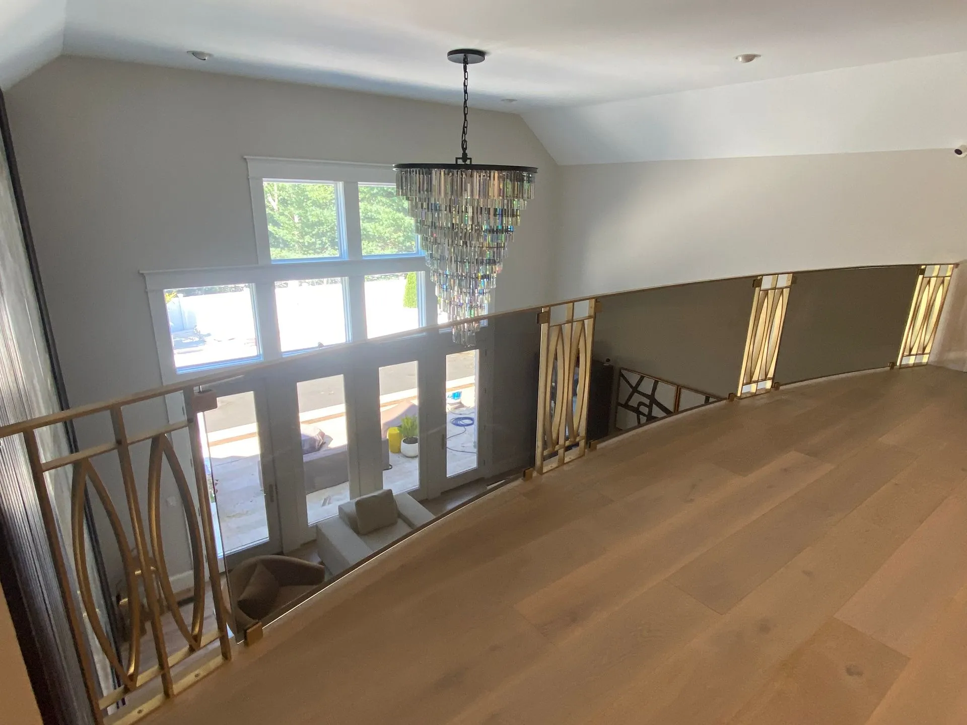 View from a balcony: gold railing, chandelier, windows, light wood flooring.