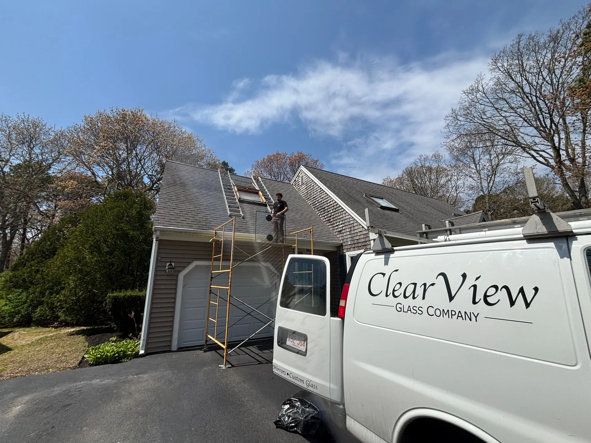 A worker on a roof near a Clear View van. Scaffolding supports the roof work. Sunny day.