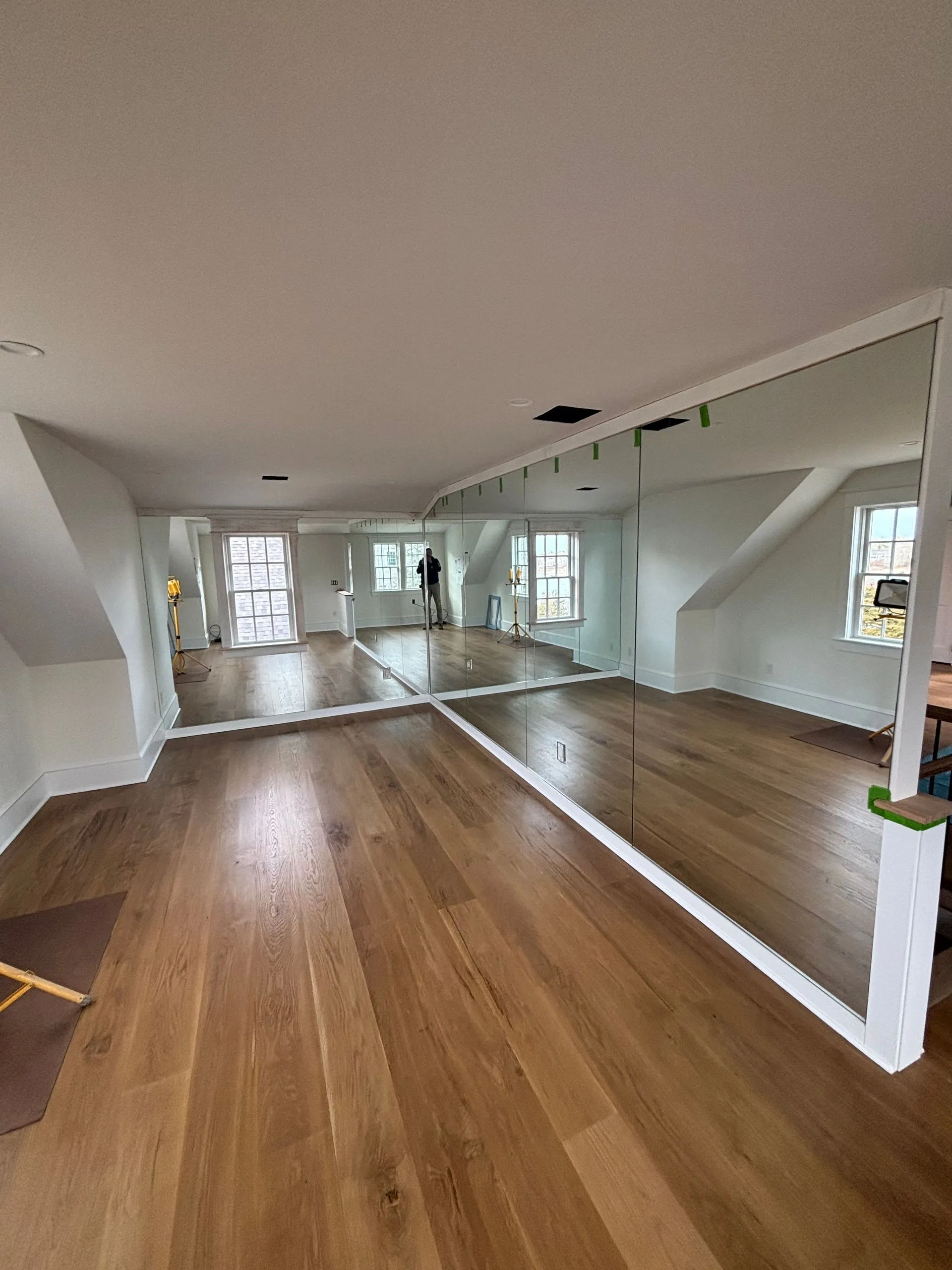 Wooden-floored room with wall-sized mirrors; white walls, slanted ceiling, and windows.