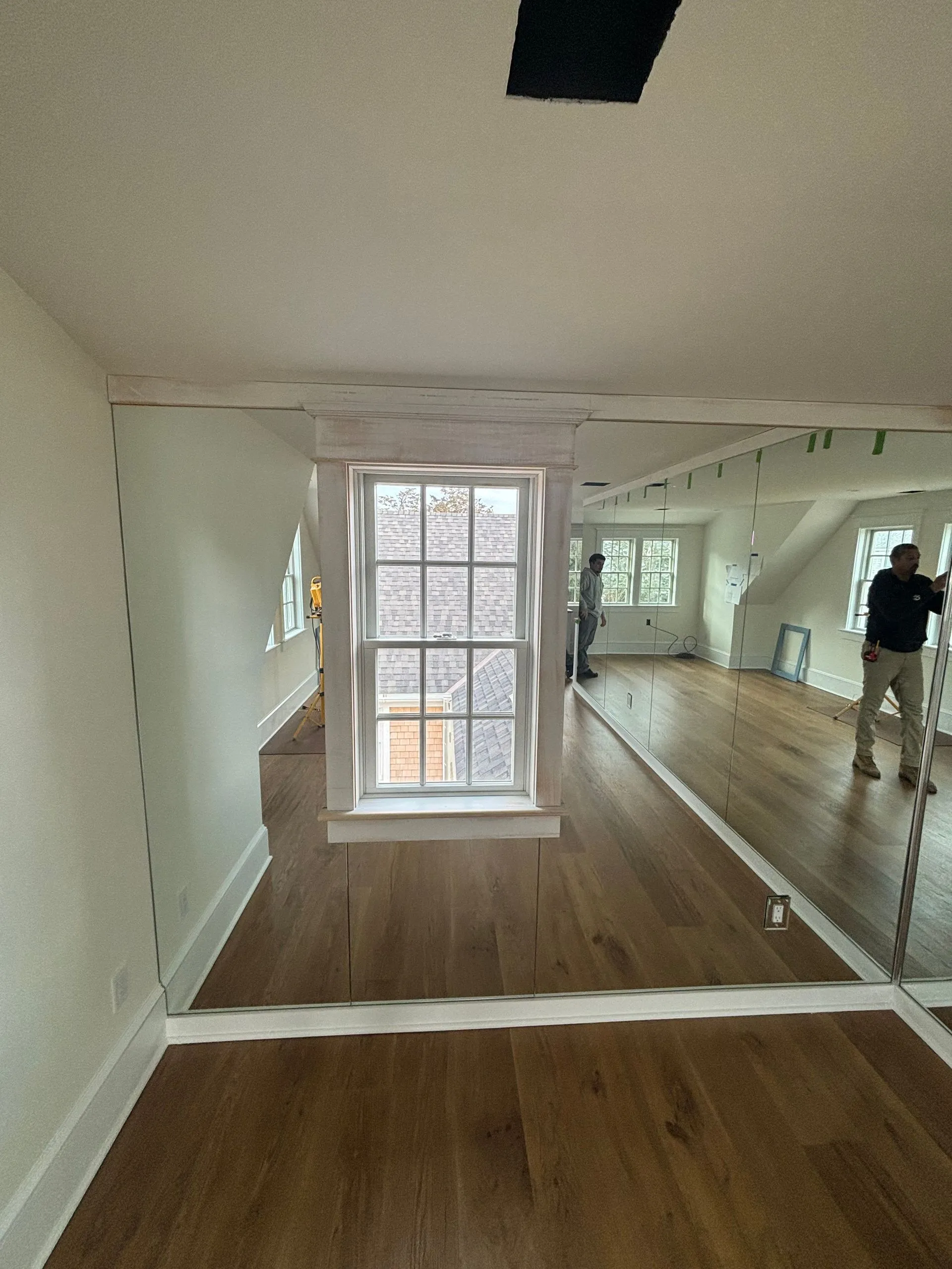 Interior room with hardwood floors, a window, and white walls. Workers in the background.