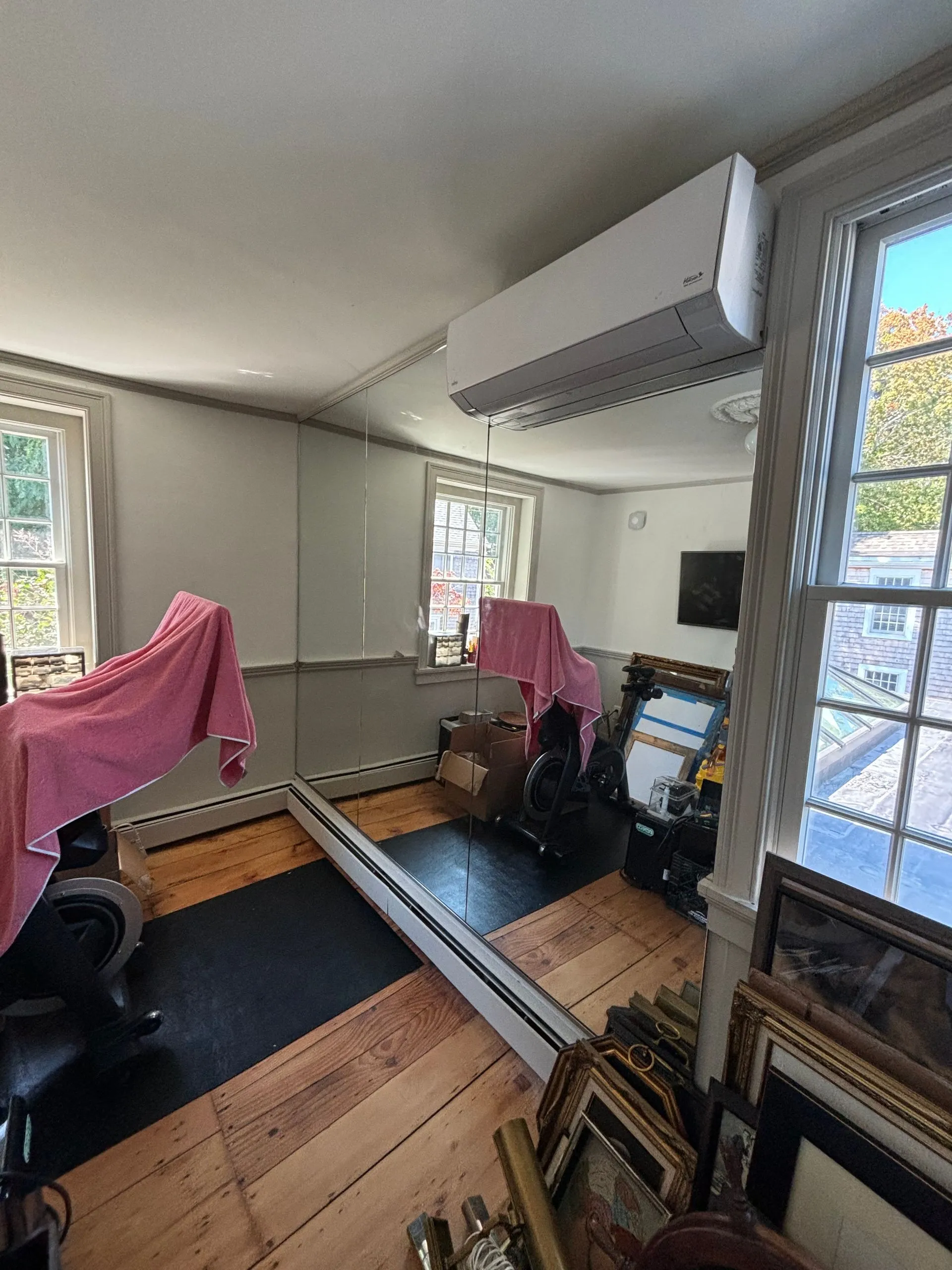 Room with air conditioner, mirror, windows, wood floor, and various items.