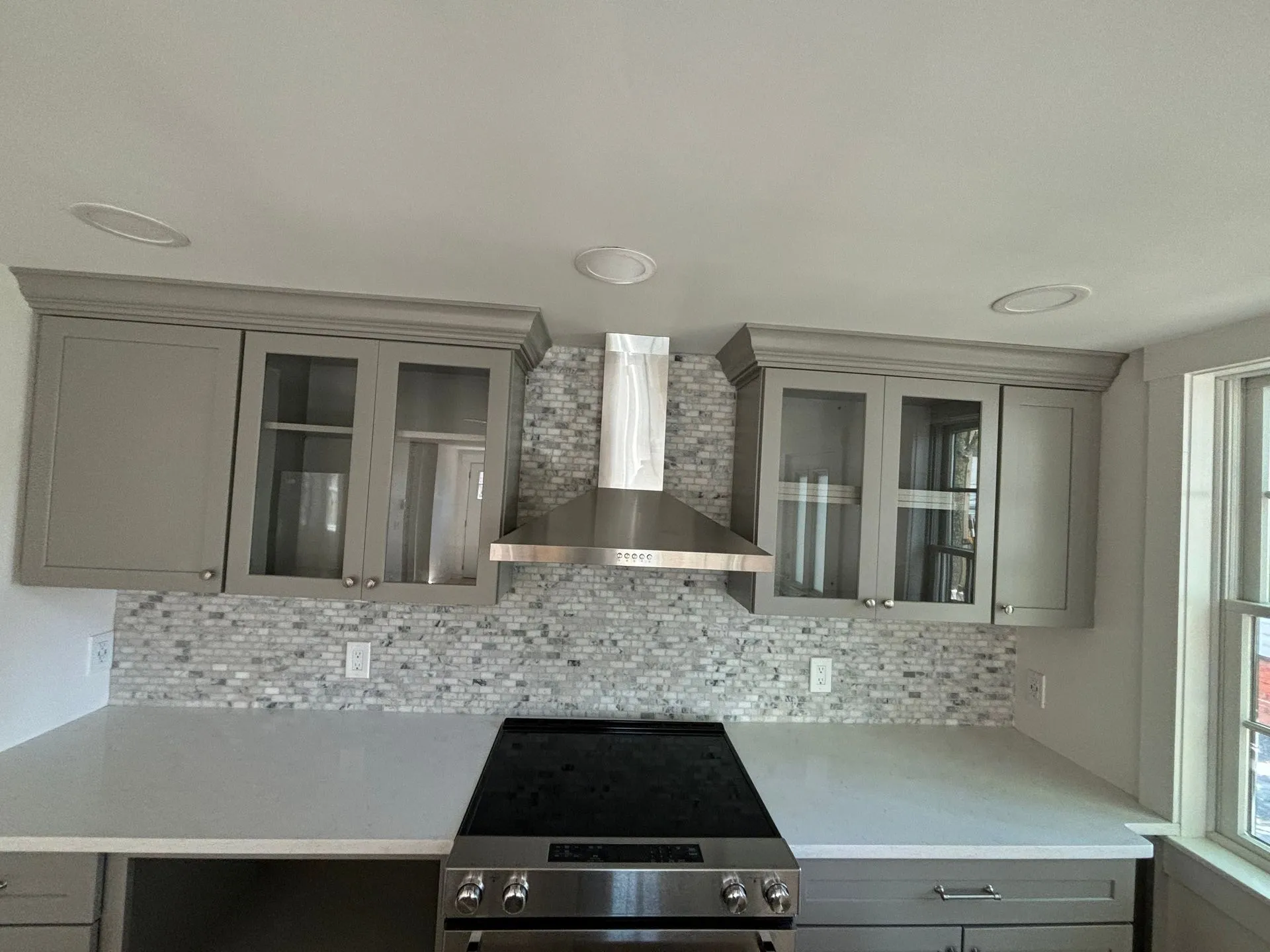 Kitchen with gray cabinets, a stainless steel range hood, and a white countertop.