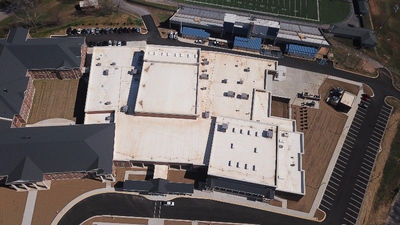 An aerial view of a large building with a football field in the background