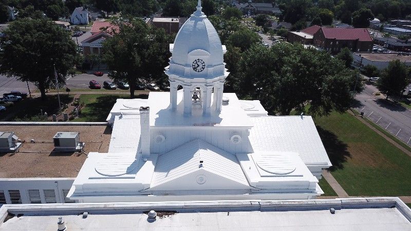 An aerial view of a white building with a dome and a clock on top