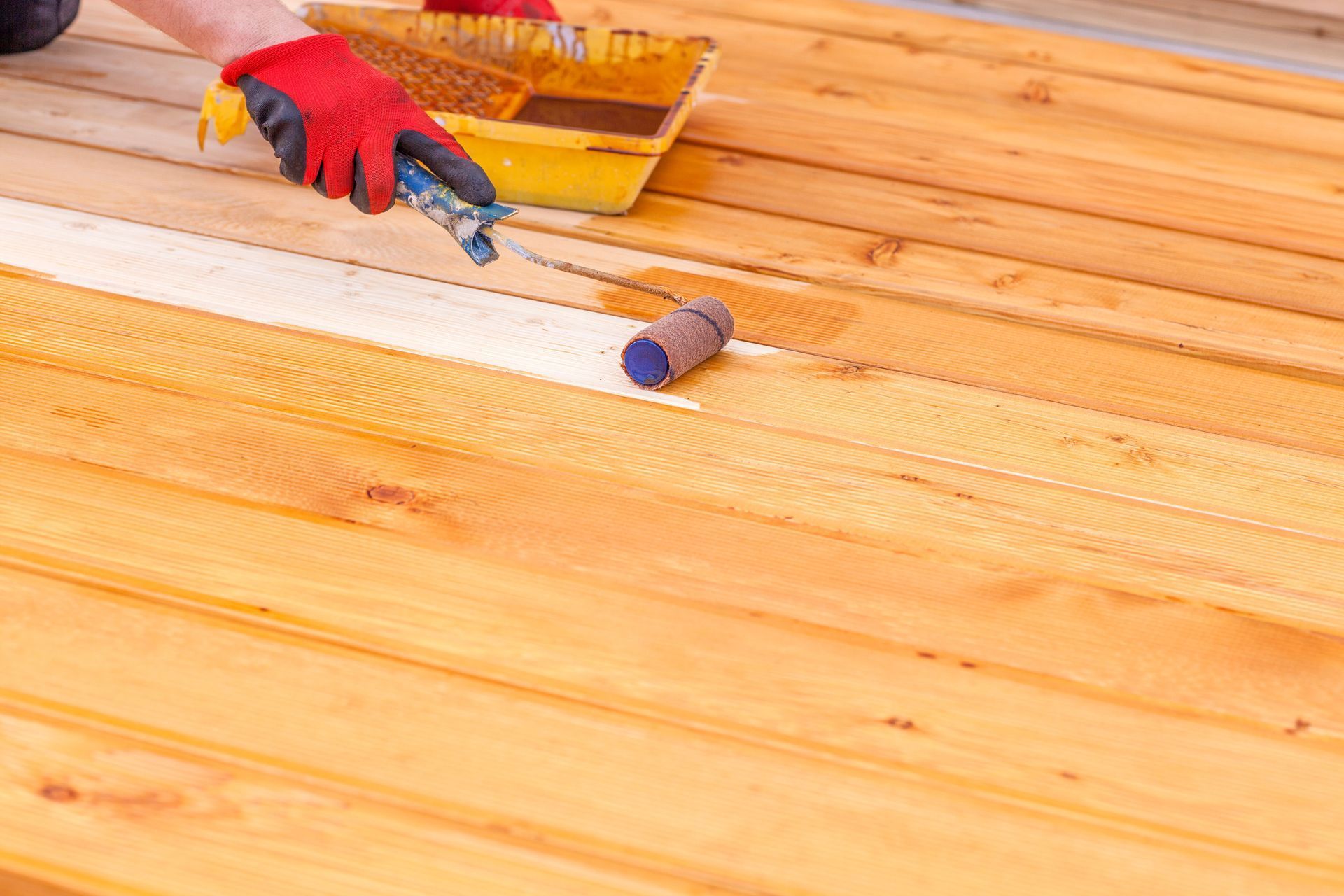 Person applying finish to a wooden floor with a paint roller and brush
