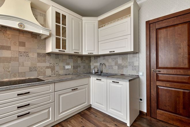 Modern kitchen corner with white cabinets, gray tile backsplash, stainless appliances, and wood flooring