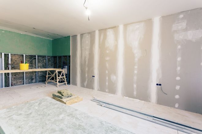 Partially renovated room with drywall, exposed floor, and workbench with tools and paint cans