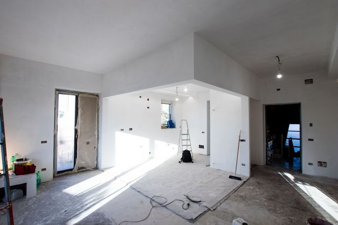 Empty white room under renovation with exposed wires, tools, and sunlight from an open doorway