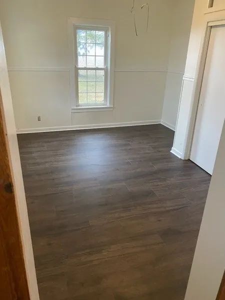 Empty room with dark wood floors, white walls, and a single window.