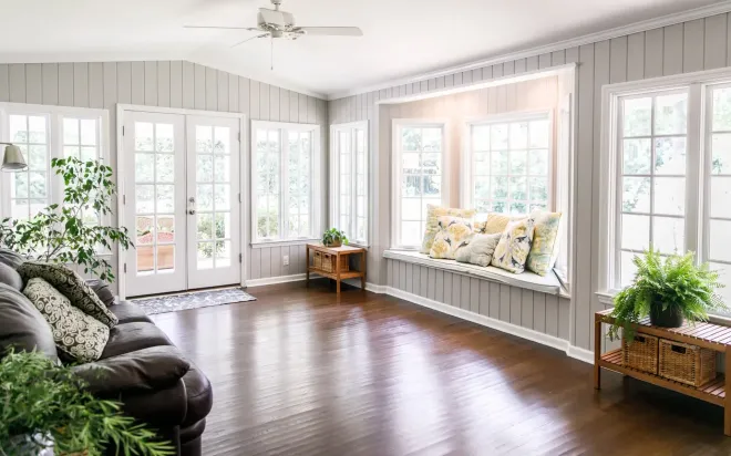 Bright sunlit living room with white French doors, hardwood floors, and potted plants