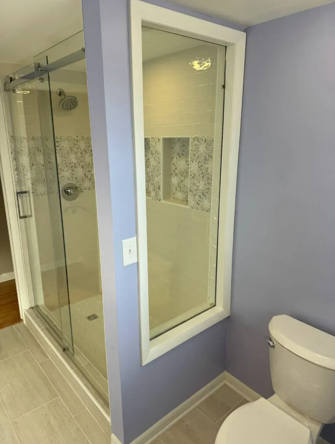 Bathroom with glass shower enclosure, lavender walls, and a toilet beside a narrow window.