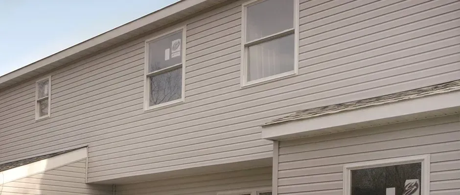 Side of a beige two-story house with vinyl siding and two upper windows