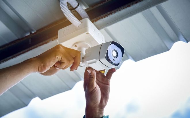 Hands installing a white LED spotlight on a ceiling beam in a bright industrial space