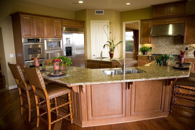 Modern kitchen with a large granite island, wood cabinets, stainless appliances, and bar stools