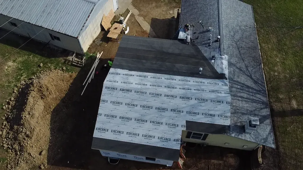 Aerial view of a house roof under construction with roofing materials and surrounding yard.