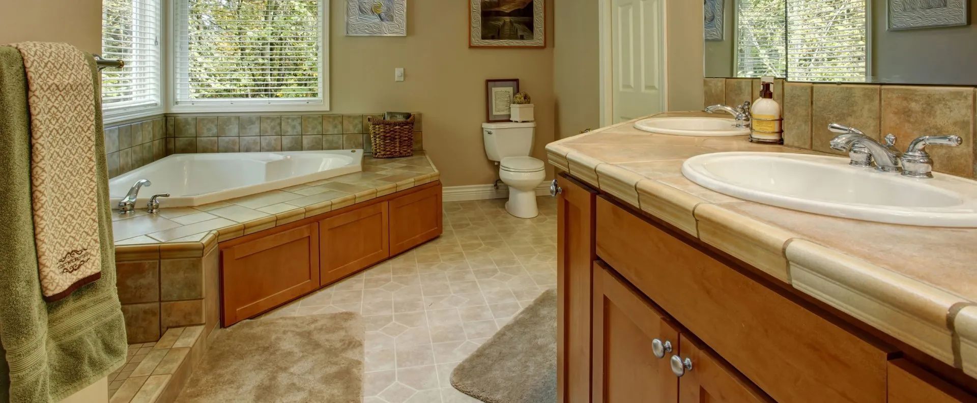 Bright bathroom with a tub, toilet, double vanity, and tiled floor by a window.