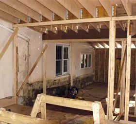 Framed interior under construction with exposed wood beams and two windows visible