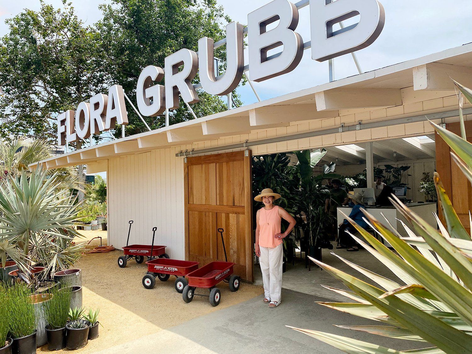 Flor de Grubb nursery entrance with potted plants and a person standing under the sign