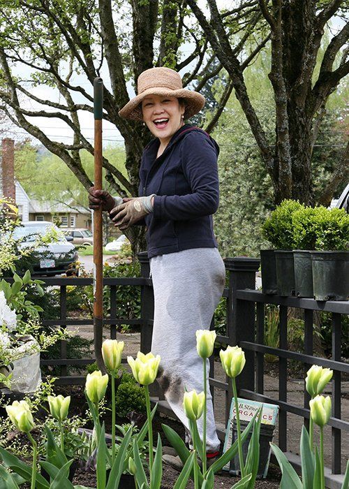Woman gardening among potted tulips, smiling in a hat and gloves outdoors