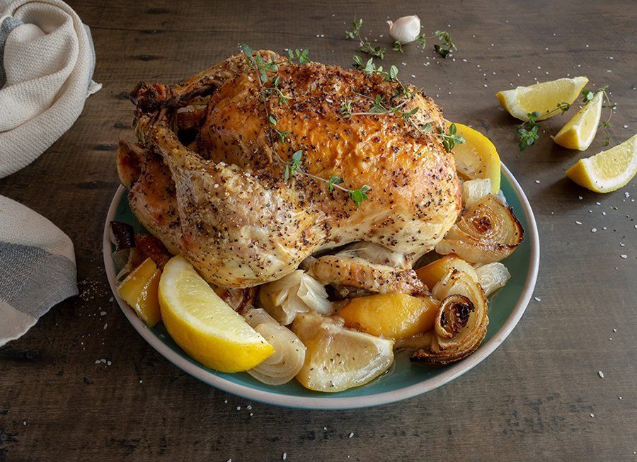 Roasted whole chicken on a plate with lemon wedges and potatoes, garnished with herbs