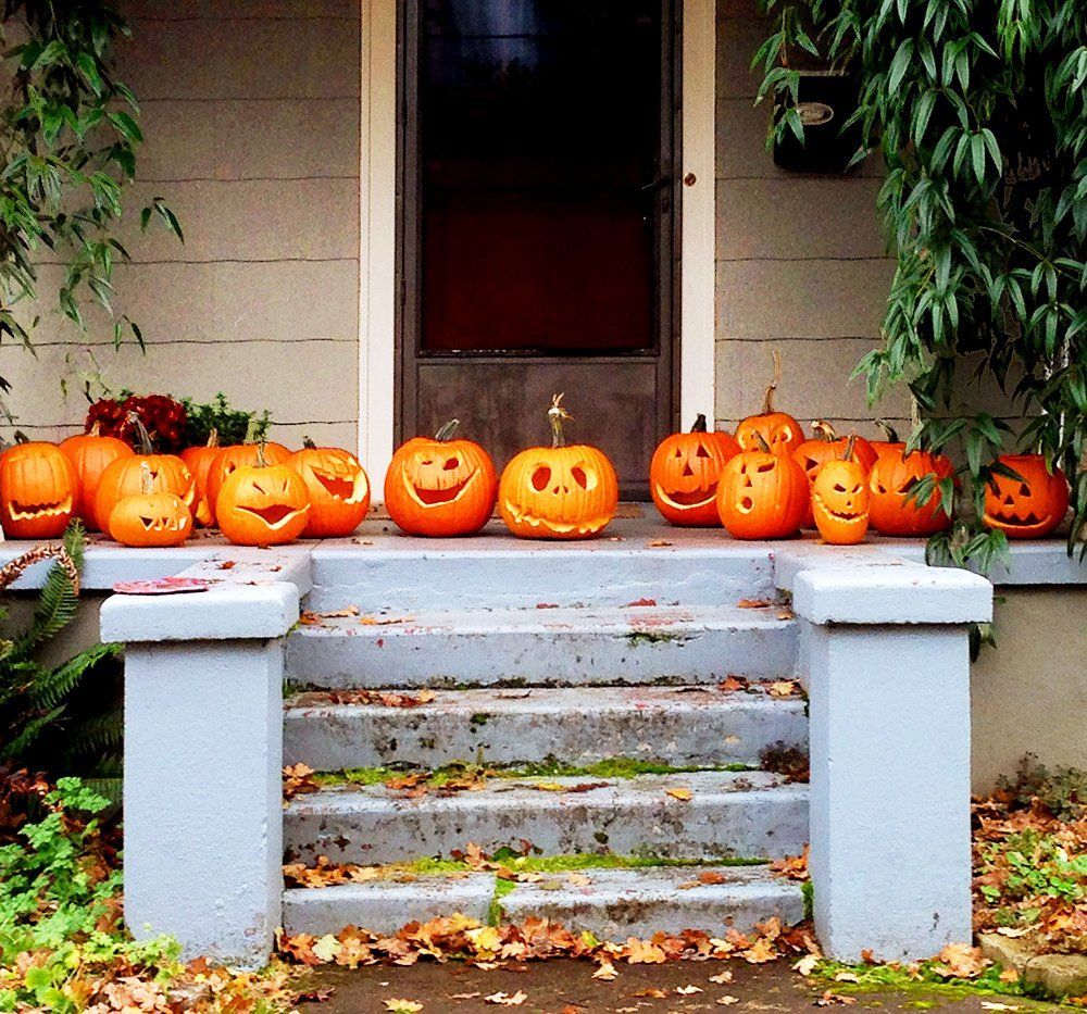 Pumpkins with carved faces lined on a porch step in front of a house