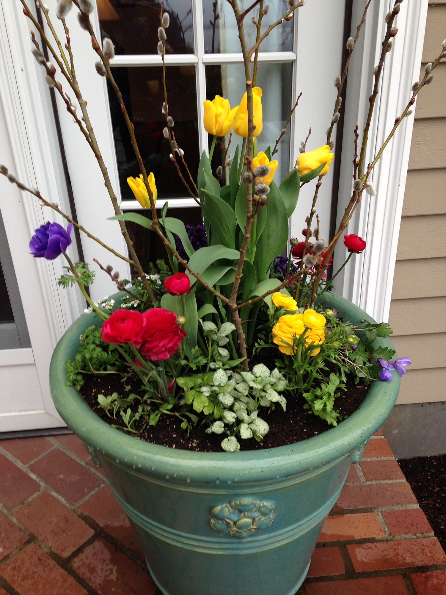 Colorful tulips and flowers in a green planter on a brick porch by a white door