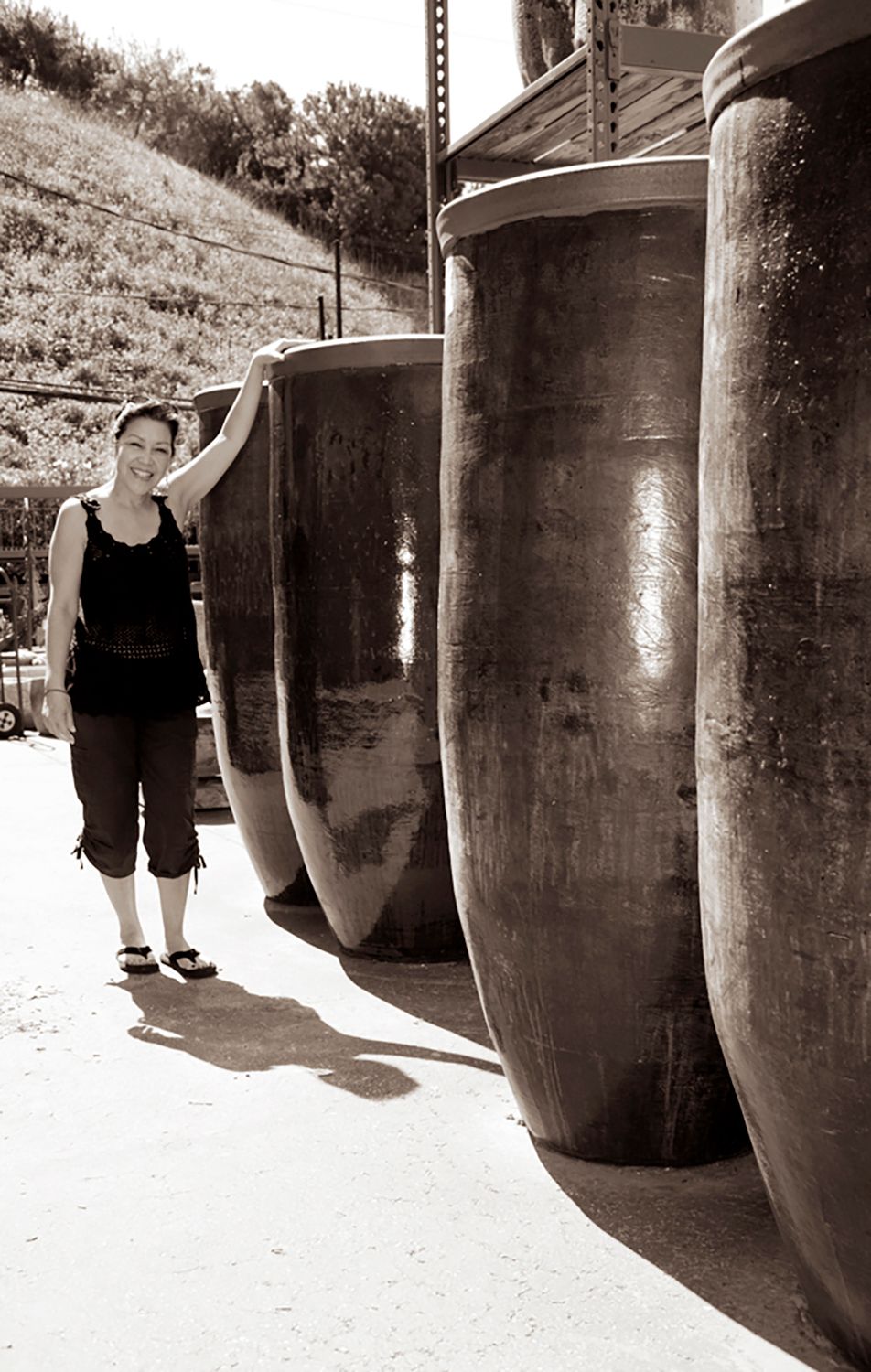 Person standing beside large upright barrels in a sunny outdoor industrial area