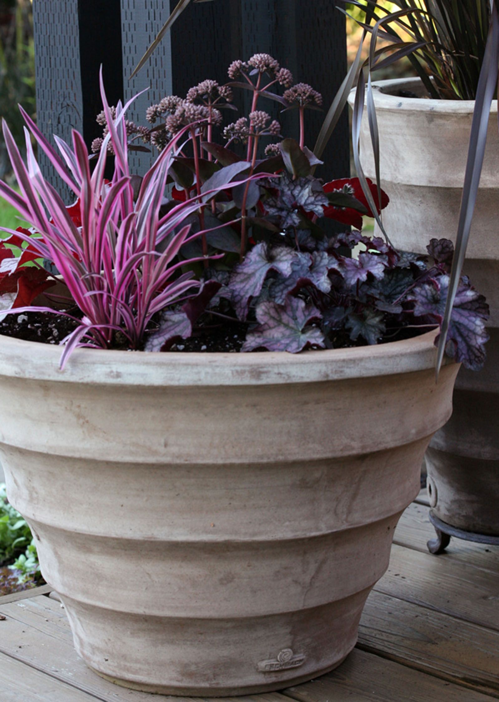 Large beige planter with pink and dark purple ornamental plants on a patio