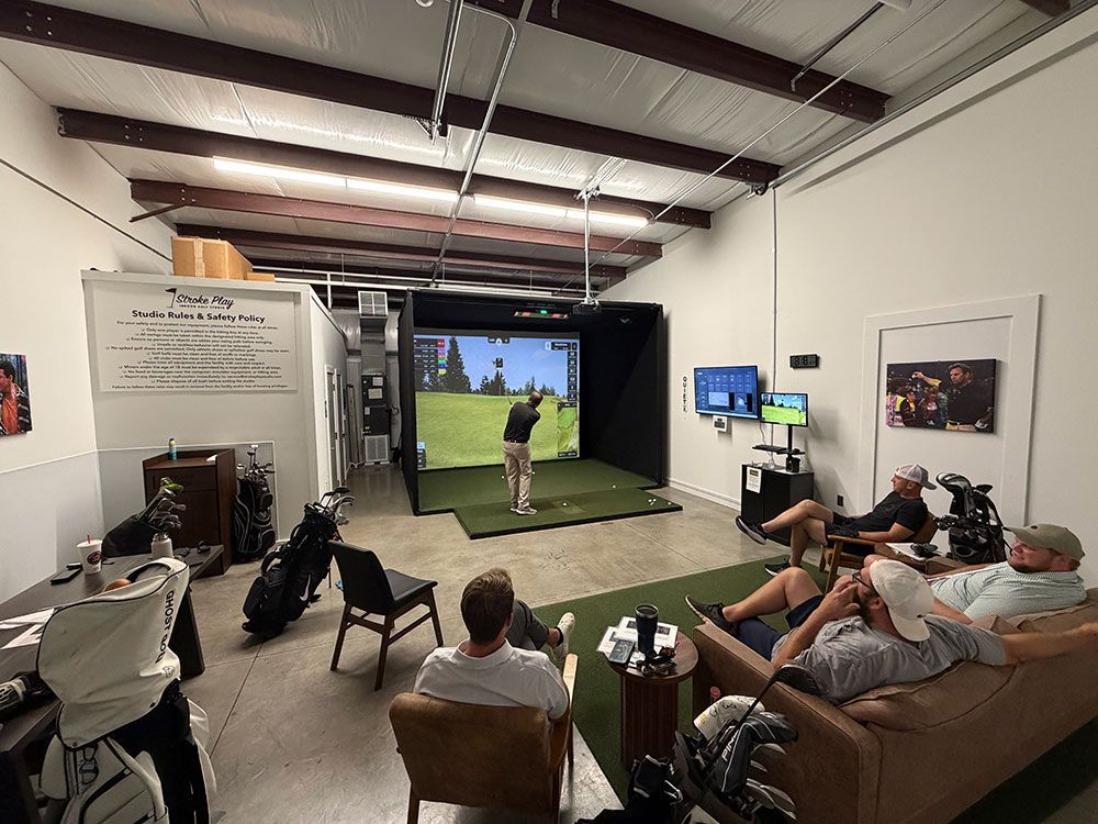 Indoor golf simulator bay with people watching a golfer hit a shot toward the screen