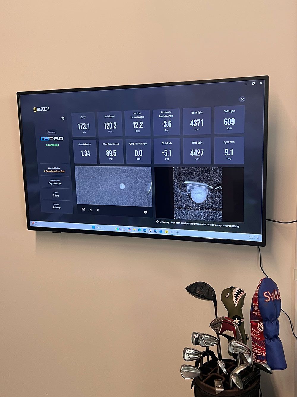 Wall-mounted TV showing a dark dashboard interface above golf clubs and a red item on a beige wall.