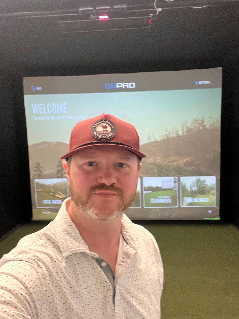 Man in a red cap taking a selfie in a dark room with a large projector screen behind him
