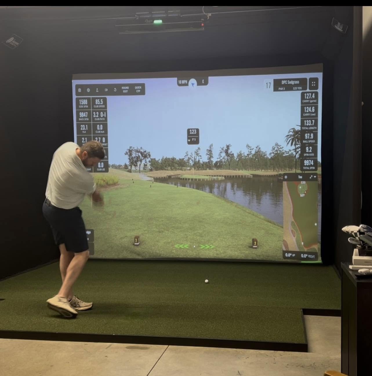 Golfer swinging indoors at a virtual driving range with a large projected fairway screen.