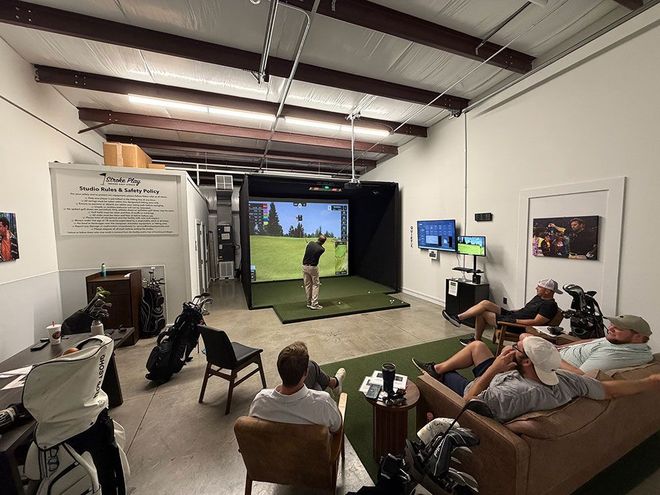 People watching a golf simulator as a golfer swings indoors in a lounge-like room