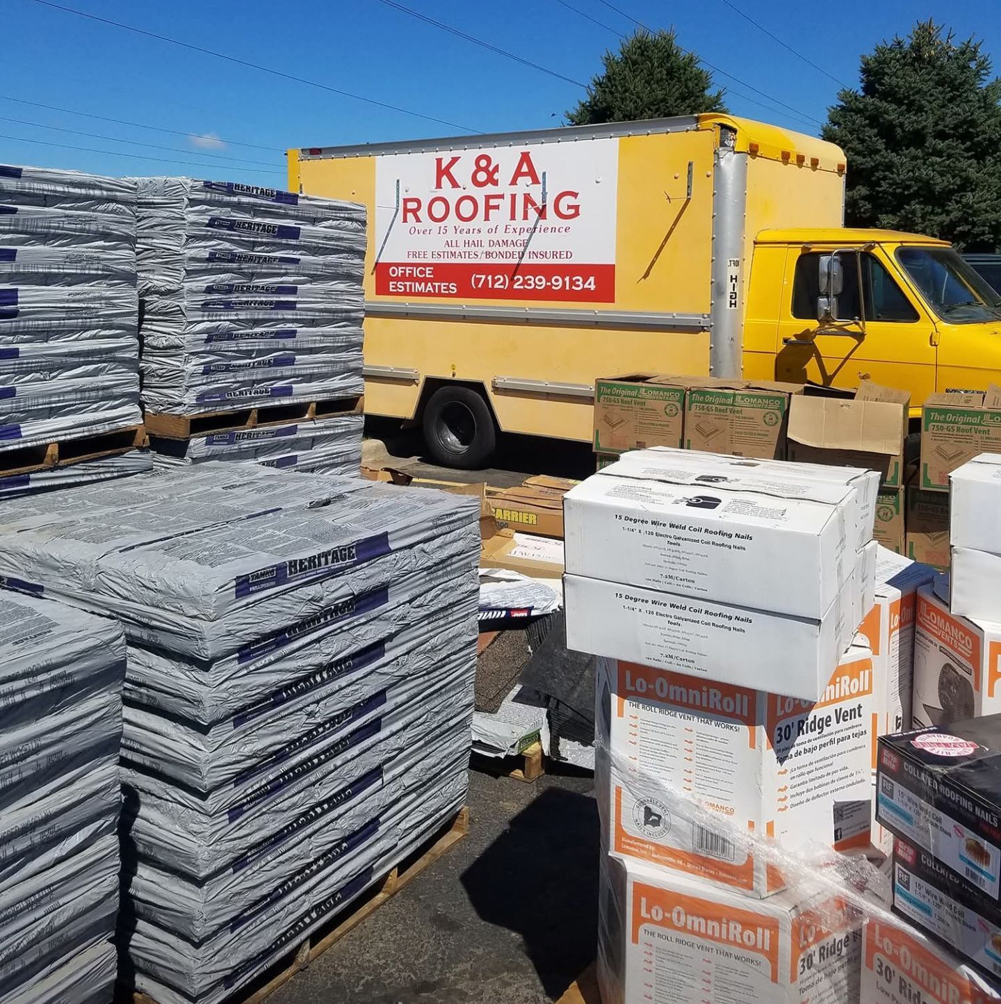Stacks of roofing materials beside a yellow K&A Roofing truck under a clear blue sky
