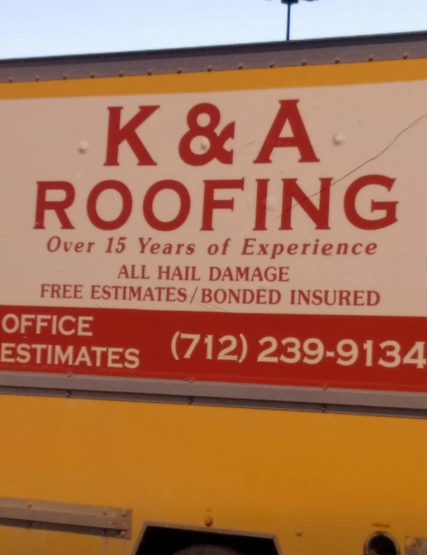 K&A Roofing sign on a yellow truck, red lettering with office estimates and phone number.