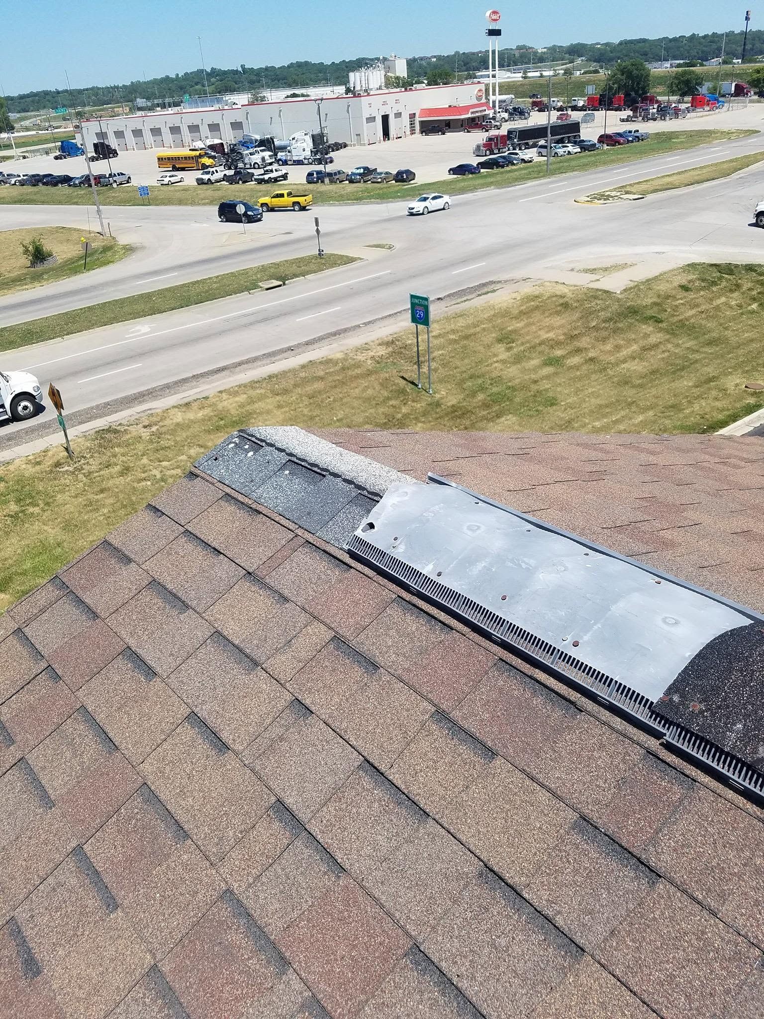 Damaged roof shingles with a torn metal patch overlooking a highway and parking lot