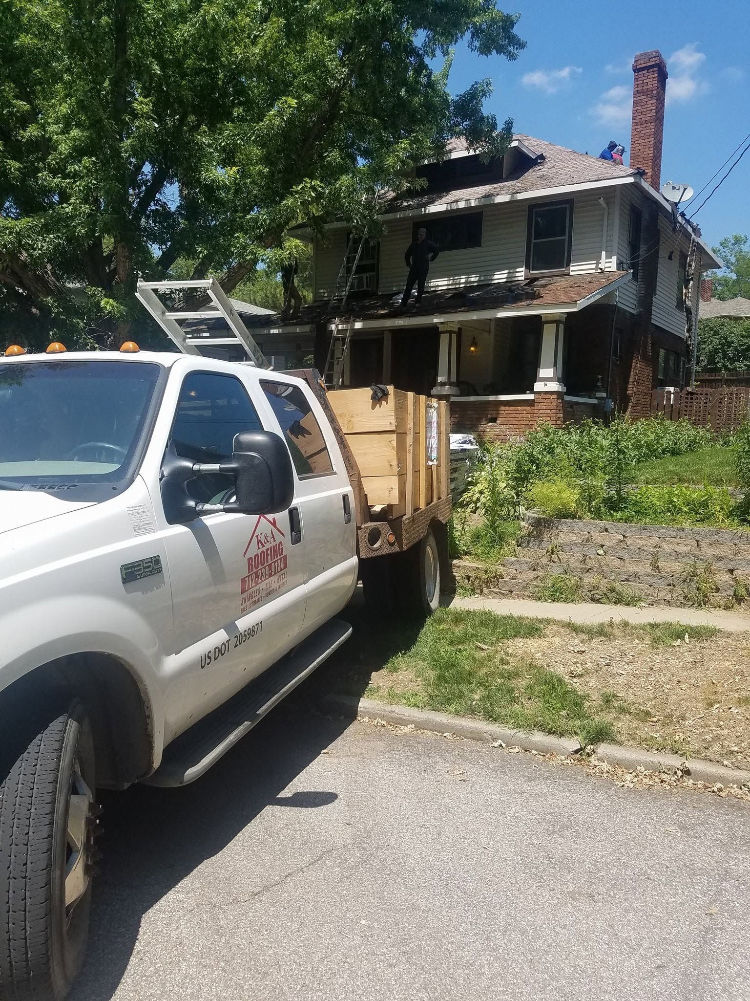 White utility truck and trailer in front of a fire-damaged house with charred upper windows and roof.