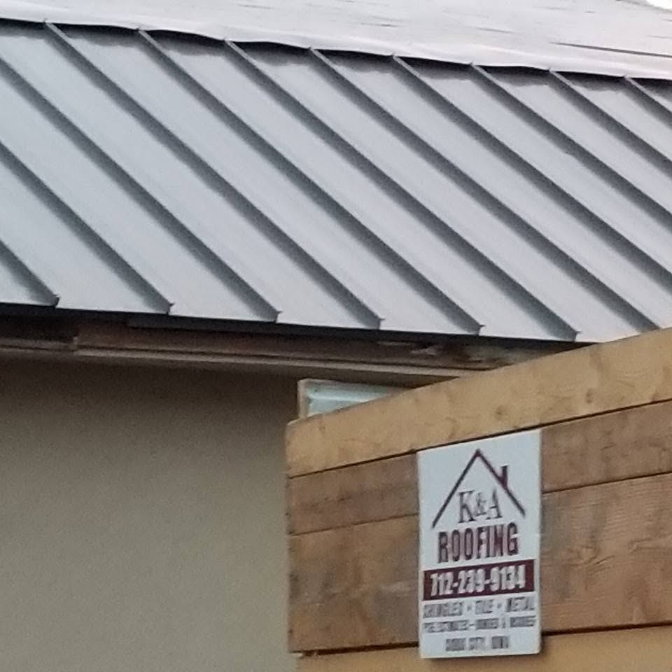 Metal roof on a building with a small roofing company sign on the wall below