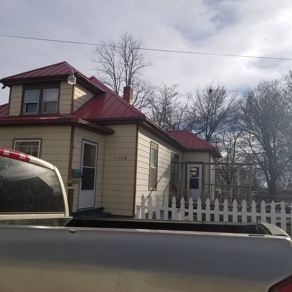Small beige house with red roof behind a white picket fence, seen beside a parked truck.