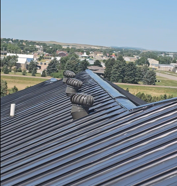 Metal roof with rooftop vents in the foreground, overlooking a suburban landscape under a clear blue sky
