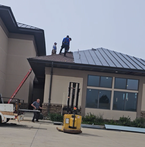 Workers on a roof installing metal roofing on a modern house, with a lift in the foreground.