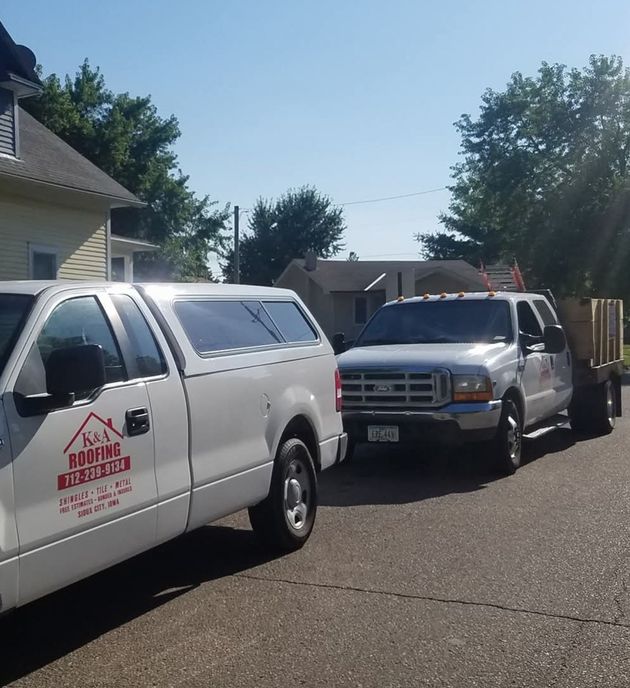 Two white service trucks parked on a sunny residential street, one with ladder rack and a red logo.